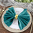 Teal velvet napkin tied with a gold ring on a decorative plate.
