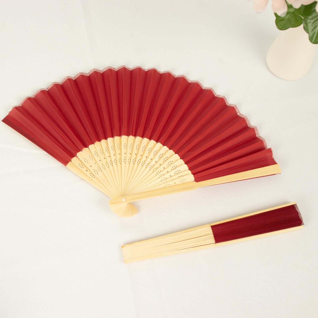 Red folding fan with bamboo handle, elegantly displayed on a white table.
