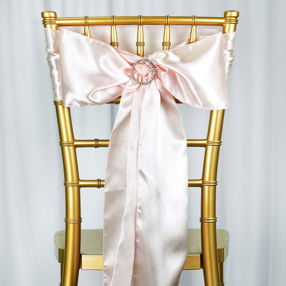Gold chiavari chair with a pink satin bow and rhinestone embellishment.
