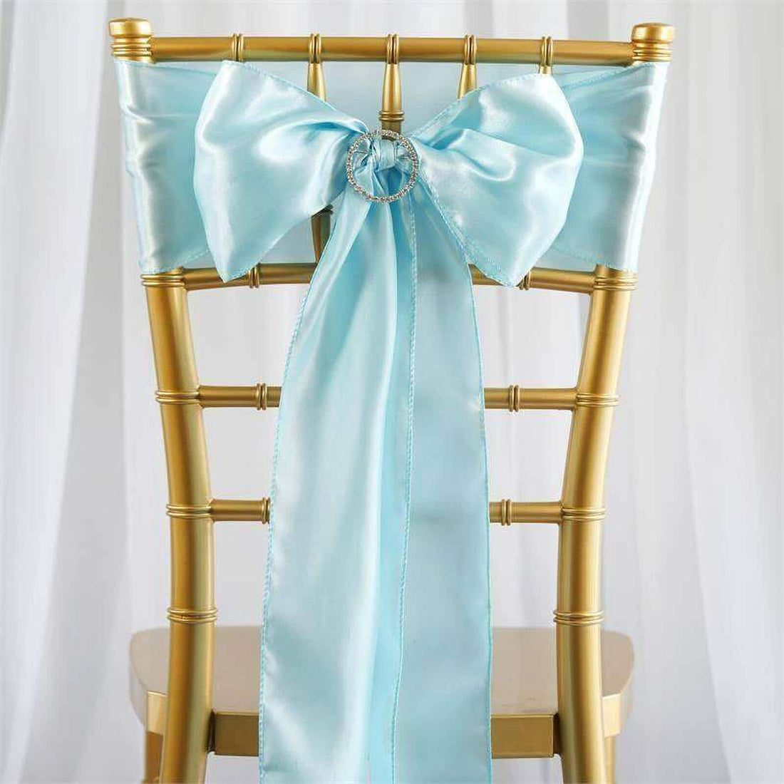 Light blue satin chair sash with bow and ring detail on a gold chair.