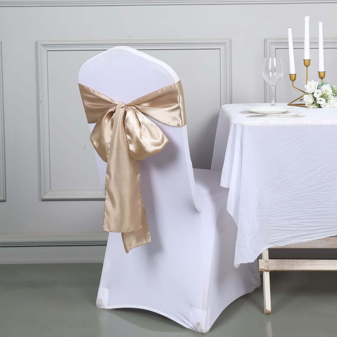 White chair cover with a gold satin bow, styled for an elegant dining setting.
