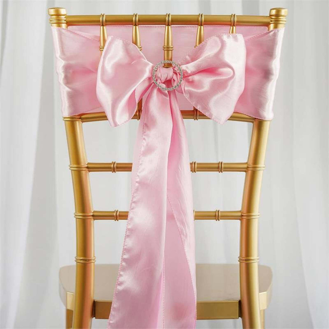 Pink satin chair sash with bow and ring detail on a gold chiavari chair.