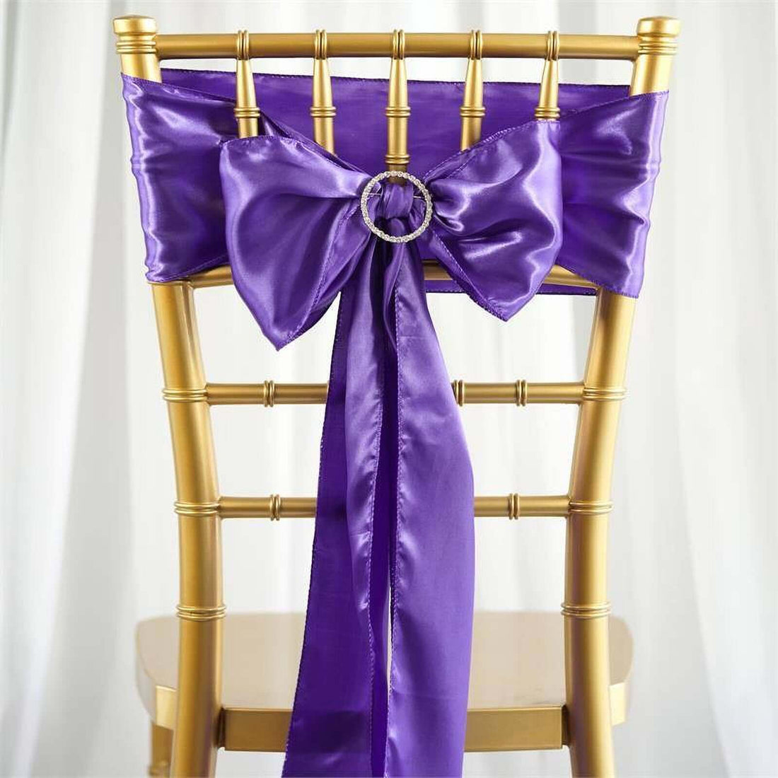 Purple satin chair sash with bow and ring on a gold chiavari chair.