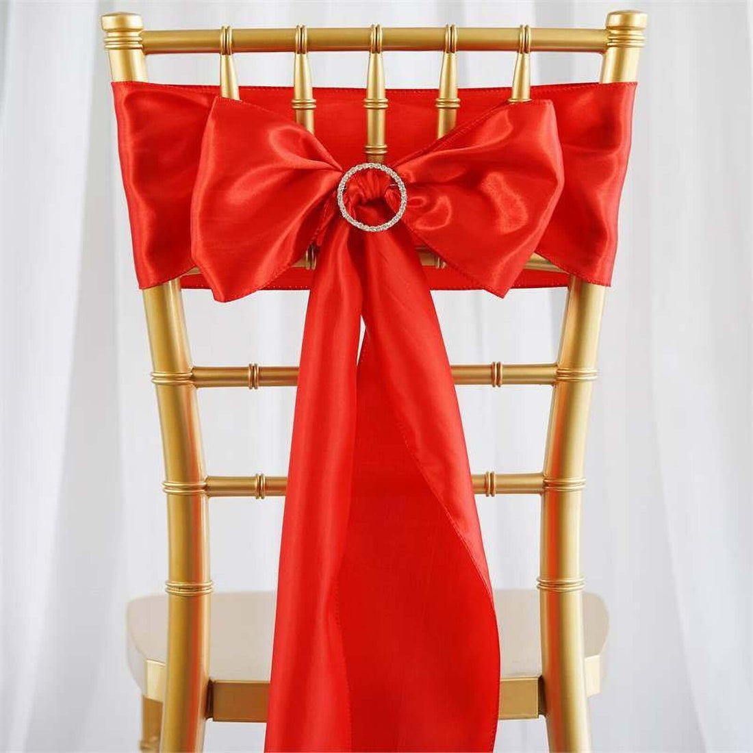 Red satin chair sash with a decorative ring, elegantly tied on a gold chair.