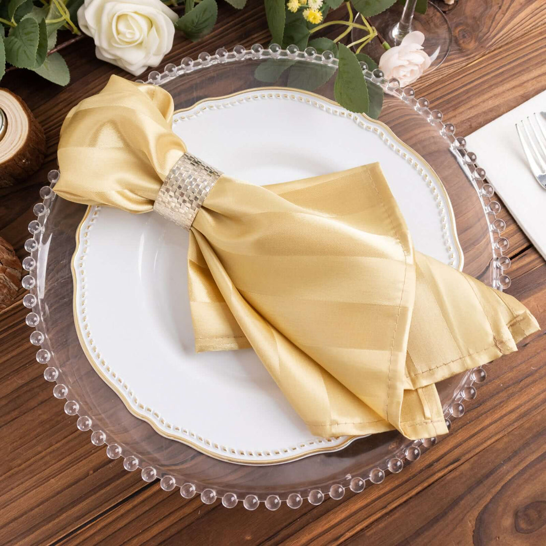 Elegant gold napkin with rhinestone ring on a decorative plate.