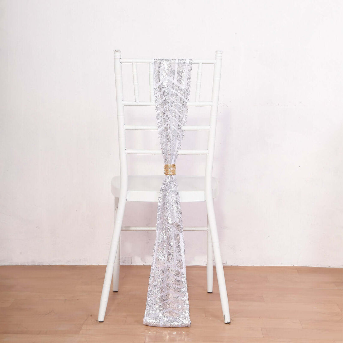 Silver sequin chair sash tied on a white chair against a plain backdrop.