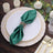 Green satin napkin with rose gold ring on an elegant dinner plate setting.