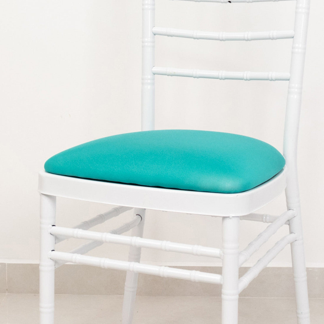 White chair with turquoise cushioned seat against a plain background.