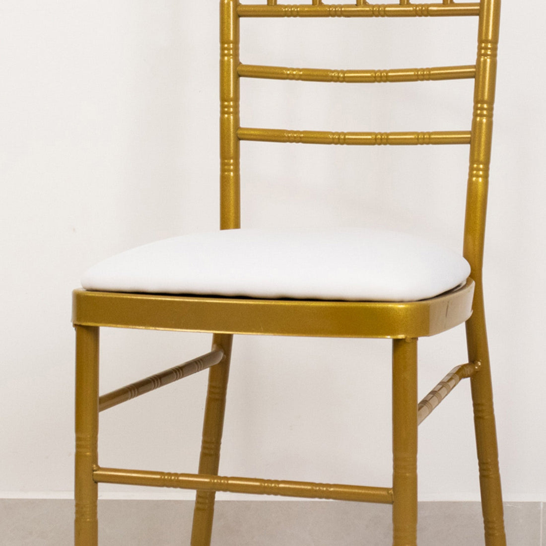 Gold chiavari chair with white cushion on a plain background