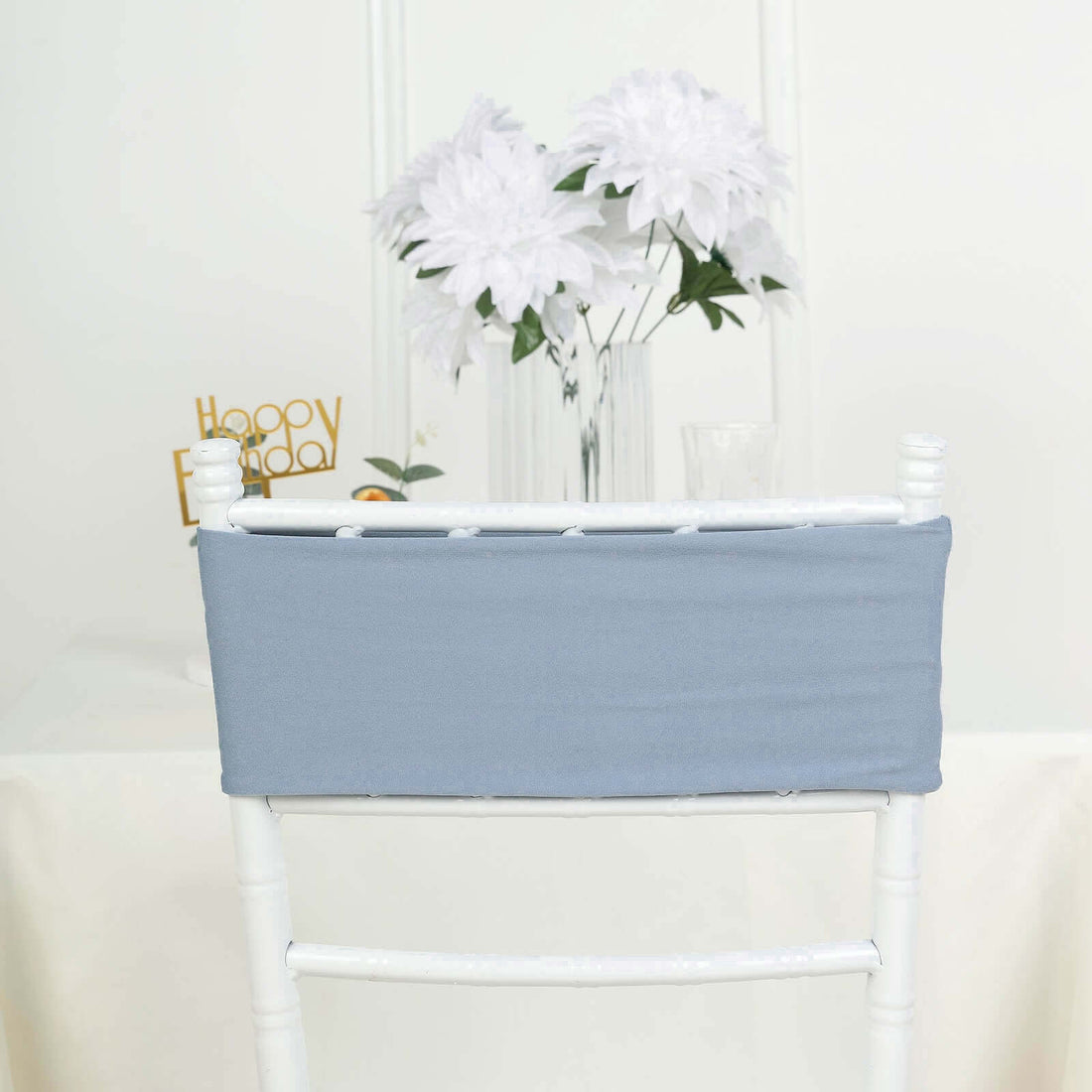 Gray chair cover on a white chiavari chair with a floral backdrop.