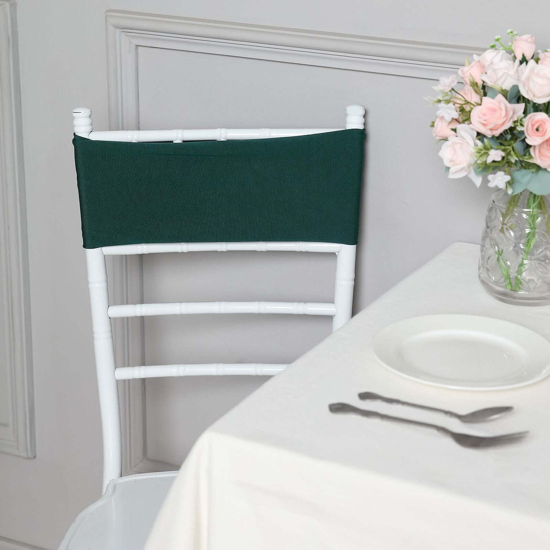 Green chair cover on a white chair beside a table with flowers and tableware.