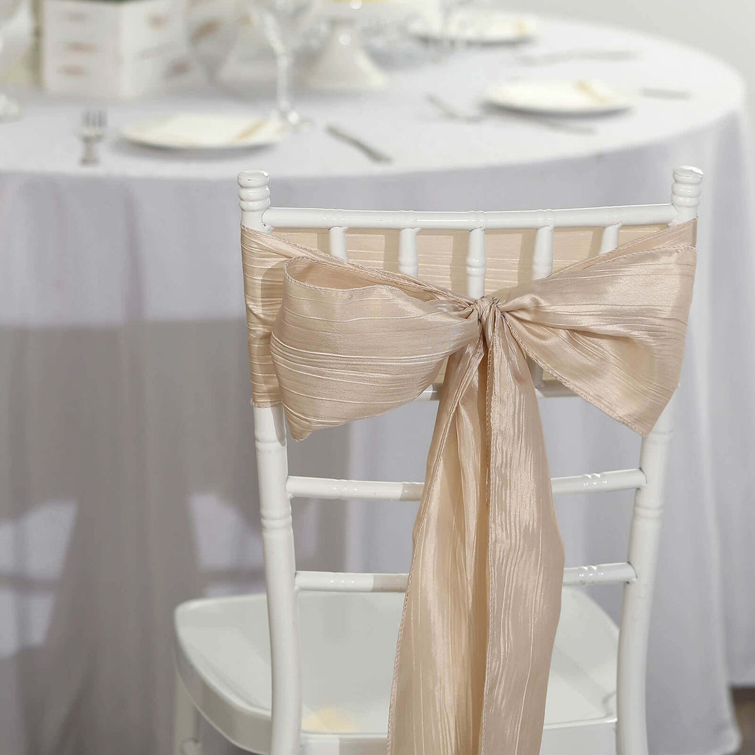 Elegant beige chair sash tied in a bow on a white chair at a dining table.