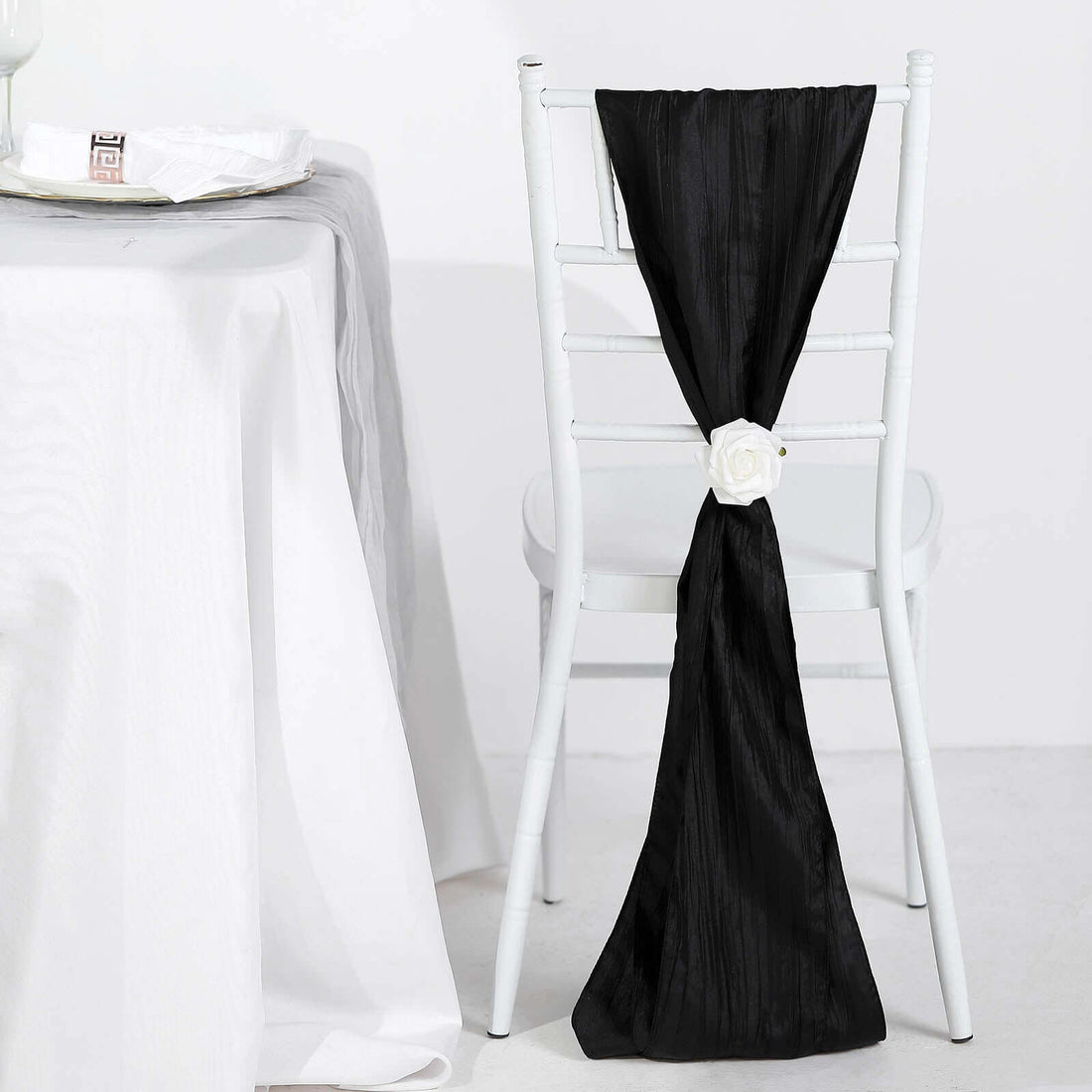 Black chair sash with white rose decoration on a white chair.