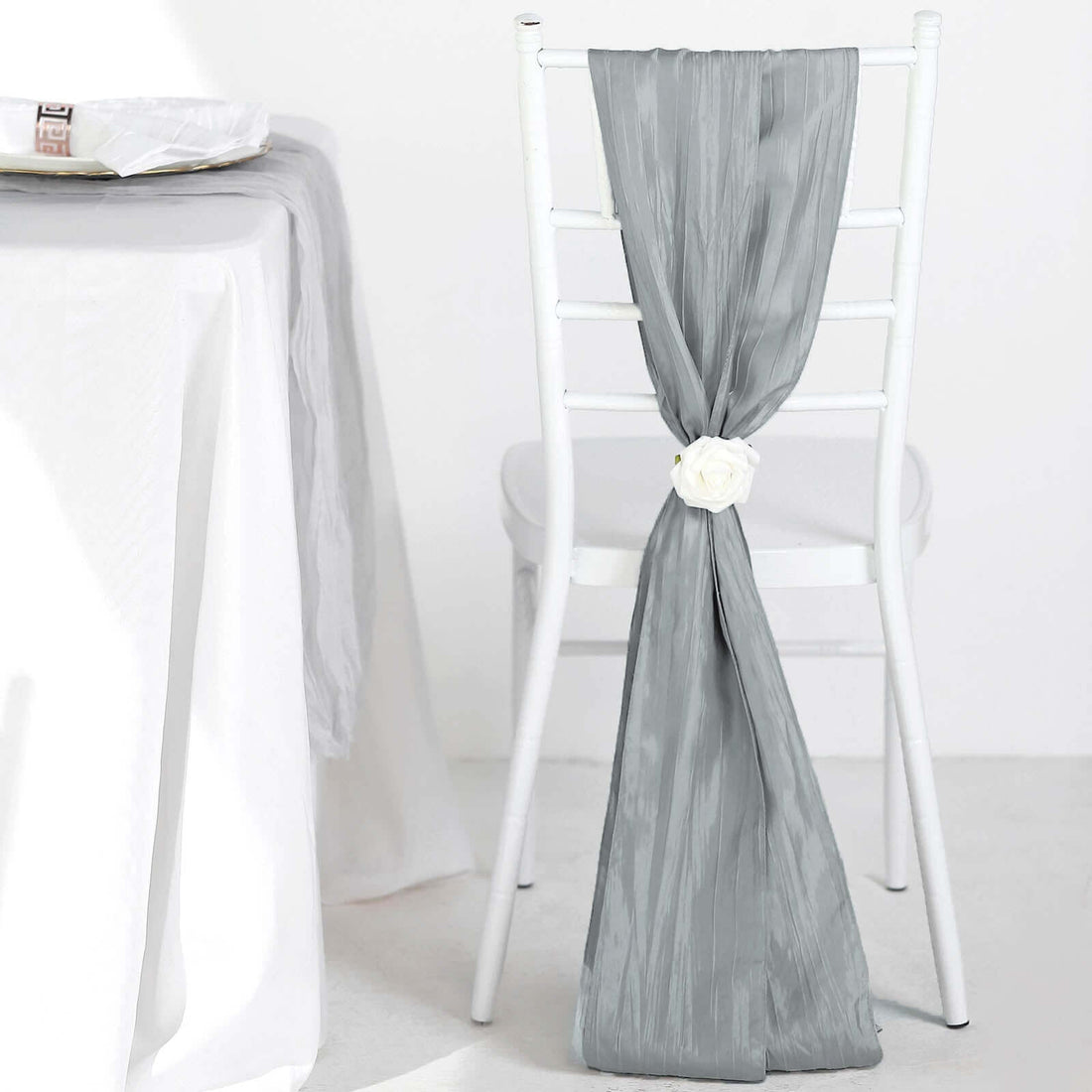 Gray table runner draped elegantly on a white chair with a decorative flower.