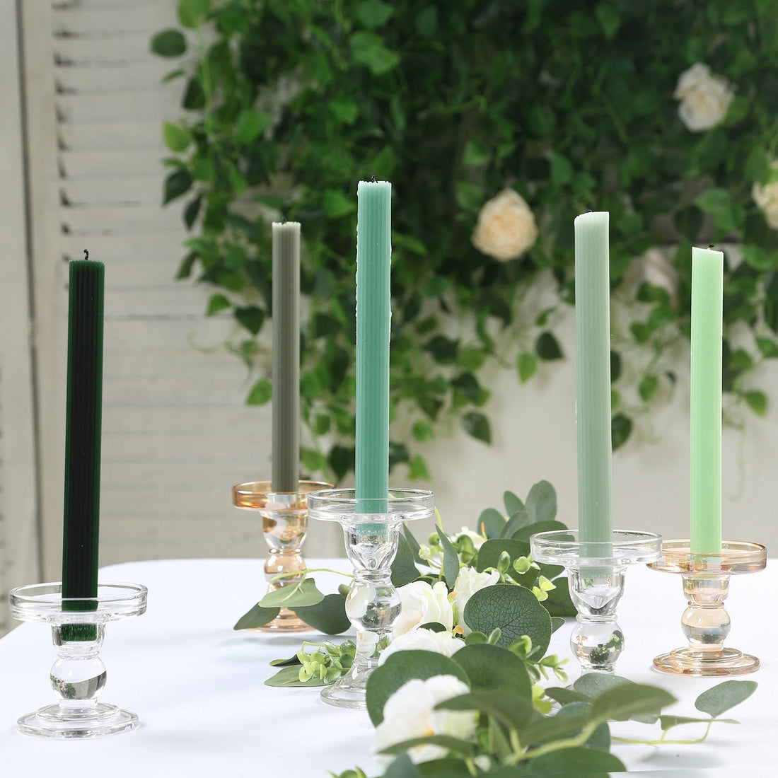 Elegant candle holders with colorful candles in a floral setting.