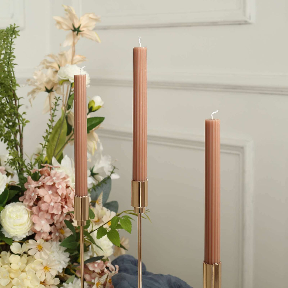 Elegant pink taper candles in gold holders, surrounded by floral arrangements.