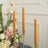 Three orange taper candles in elegant holders against a floral arrangement.