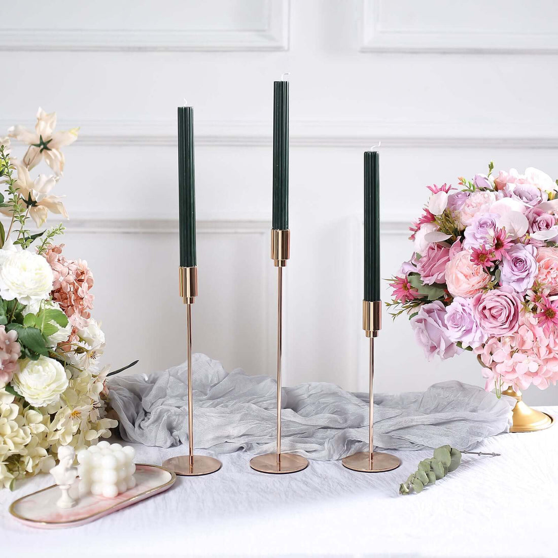 Elegant candle holders with green candles, surrounded by floral arrangements.