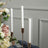 White candlesticks in elegant holders with floral backdrop.