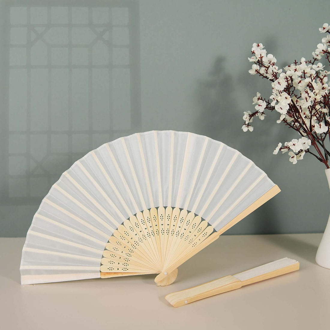 Elegant white folding fan with wooden handle displayed next to a vase of flowers.