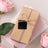 Gift box wrapped in brown paper with twine, surrounded by pink roses and stationery.
