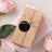 Gift box wrapped in brown paper with twine and a black tag, surrounded by pink roses.