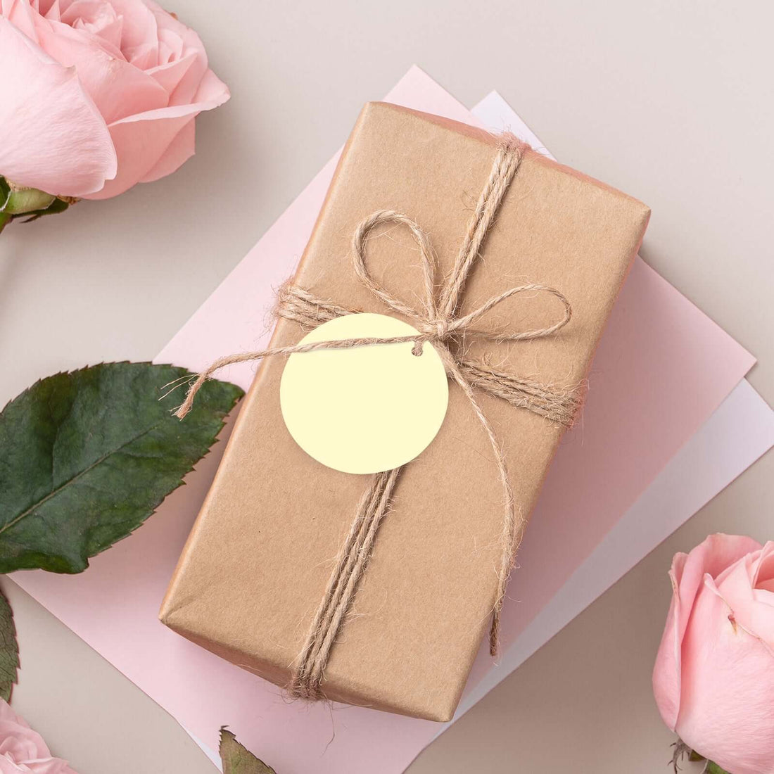 Gift box wrapped in brown paper with a tag, surrounded by pink roses.