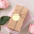 Gift box wrapped in brown paper with a tag, surrounded by pink roses.