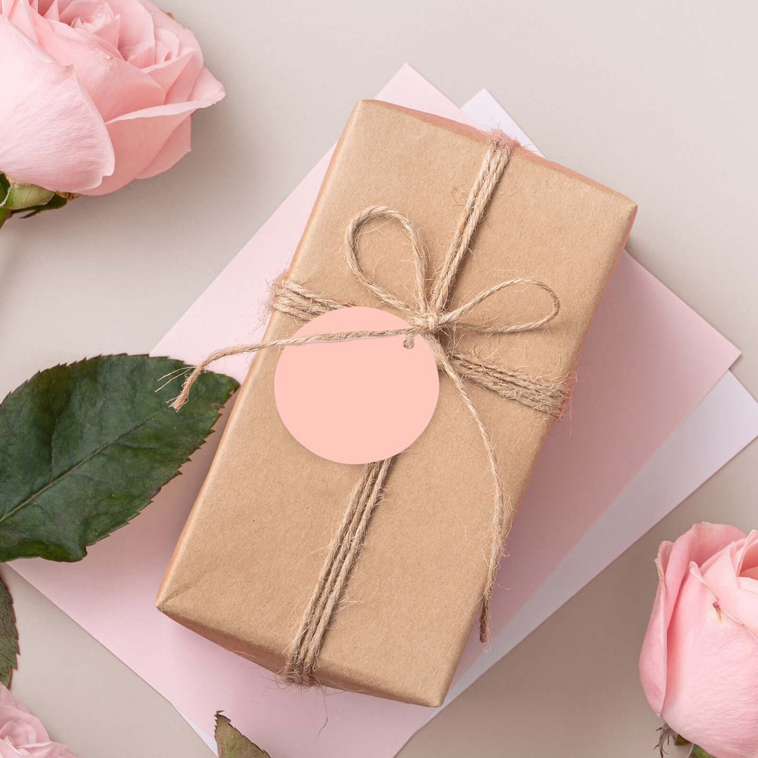 Brown gift box with twine and tag, surrounded by pink roses and paper.