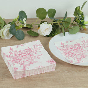 Pink floral napkins stacked beside a plate and greenery on a wooden surface.