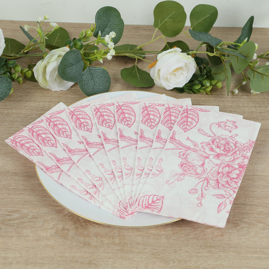 Decorative pink floral napkins arranged on a plate with greenery background.