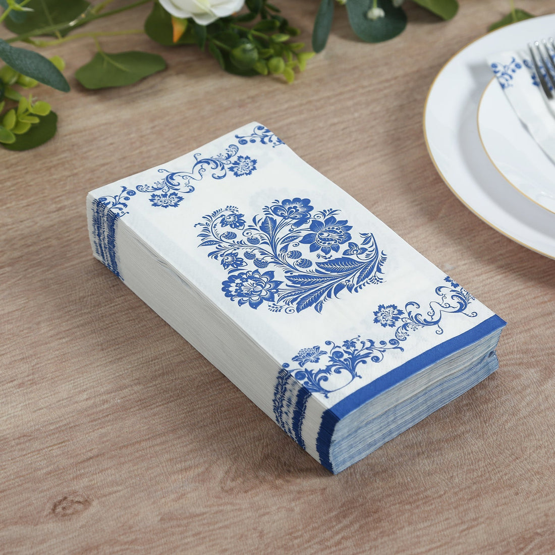 Decorative blue and white floral napkins stacked on a wooden table.