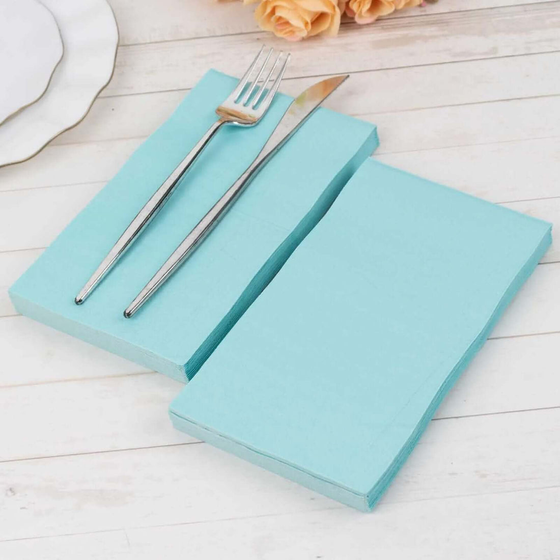 Light blue paper napkins with a silver fork and knife on a wooden table.