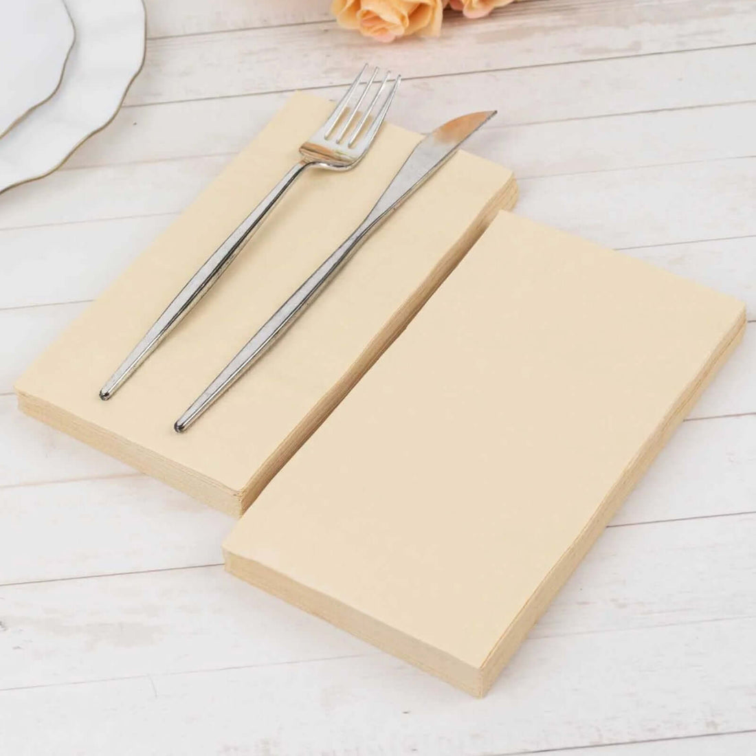 Beige dinner napkins with fork and knife on a wooden table.