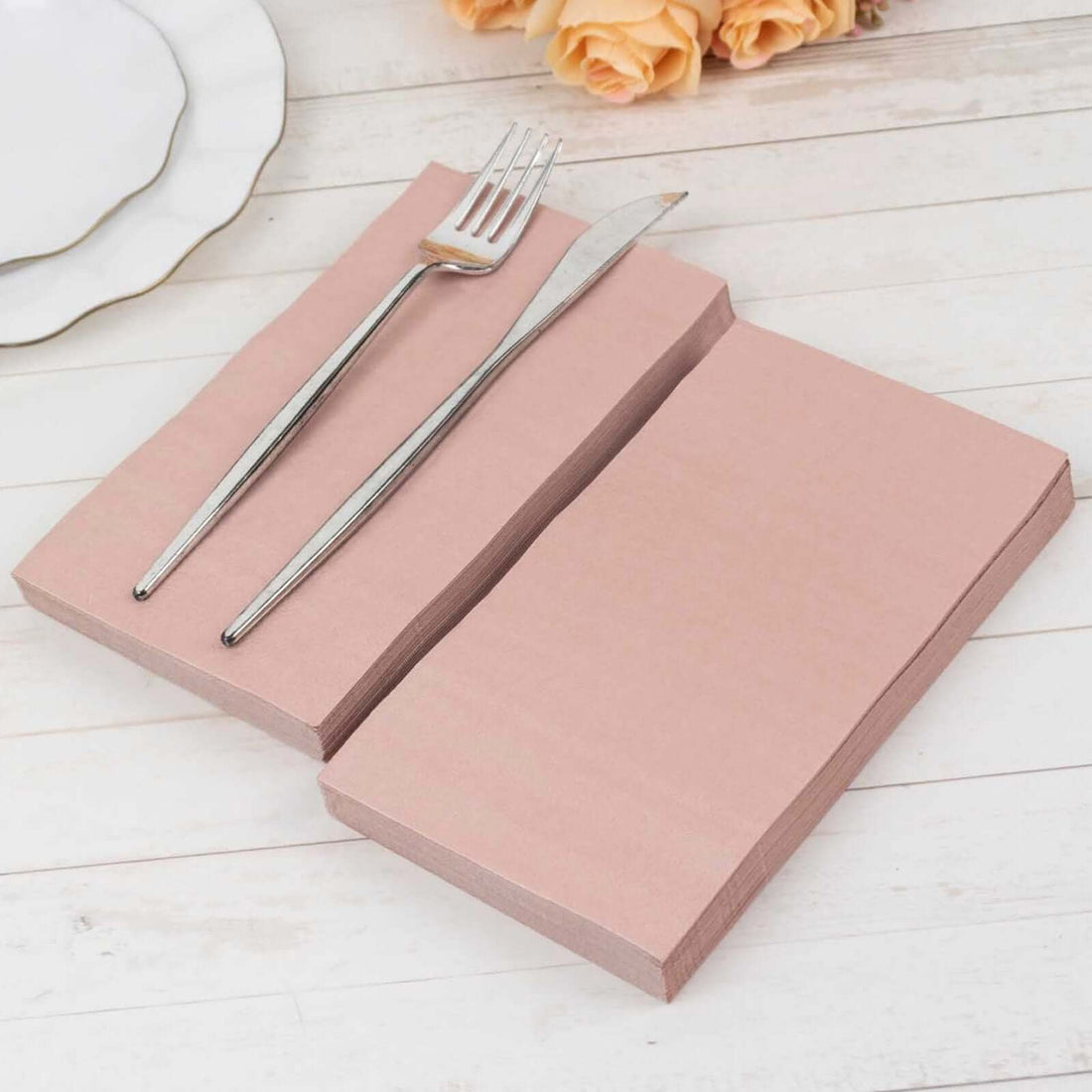 Pink napkins with silver fork and knife on a rustic wooden table.
