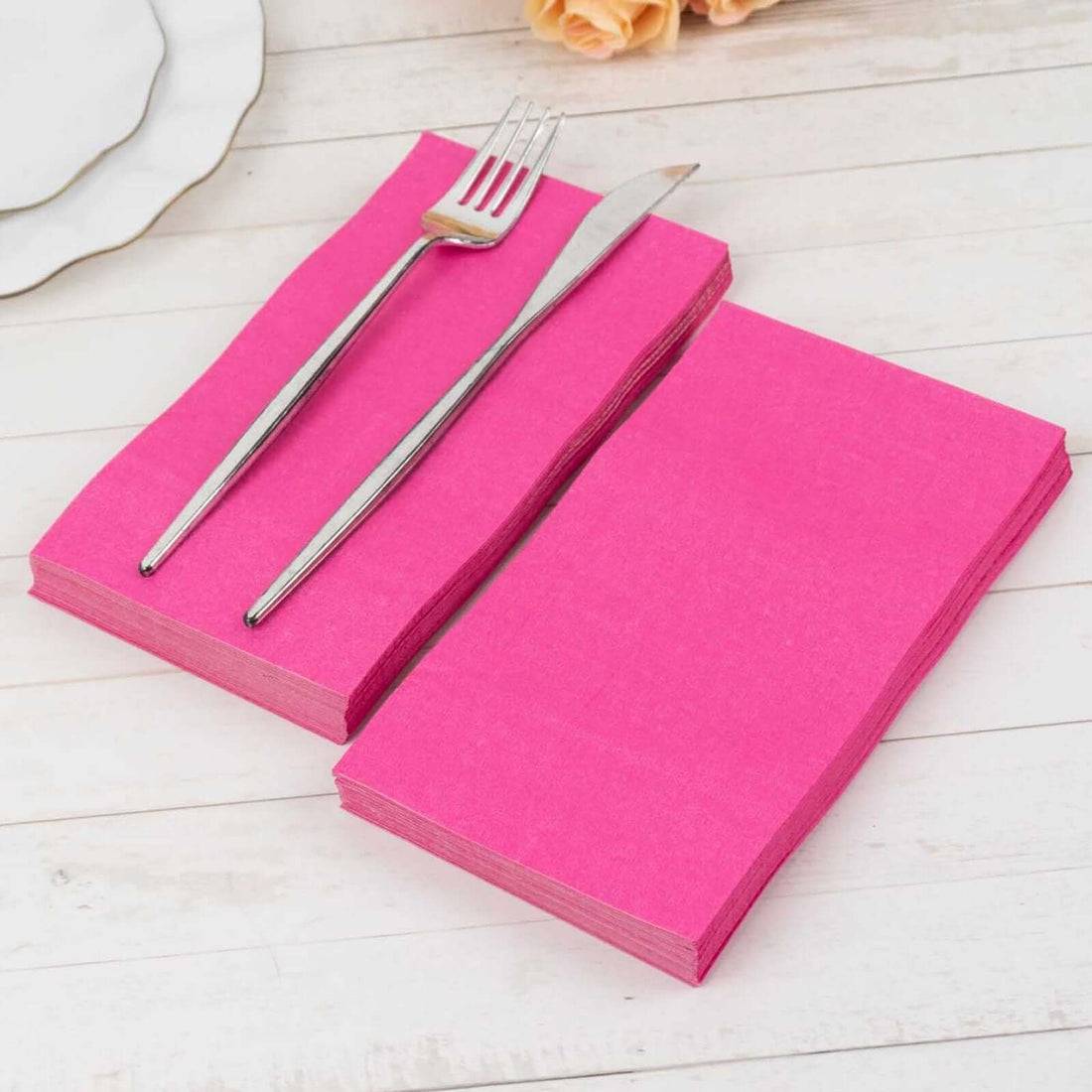 Pink disposable napkins with silver fork and knife on a wooden table.