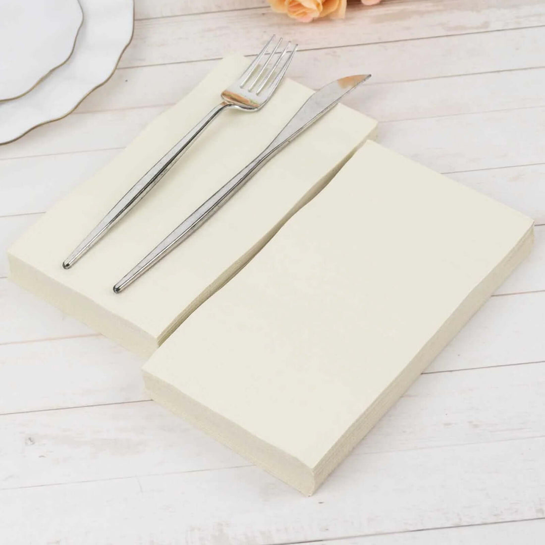 Elegant cream-colored napkins with silver fork and knife on a rustic wooden table.