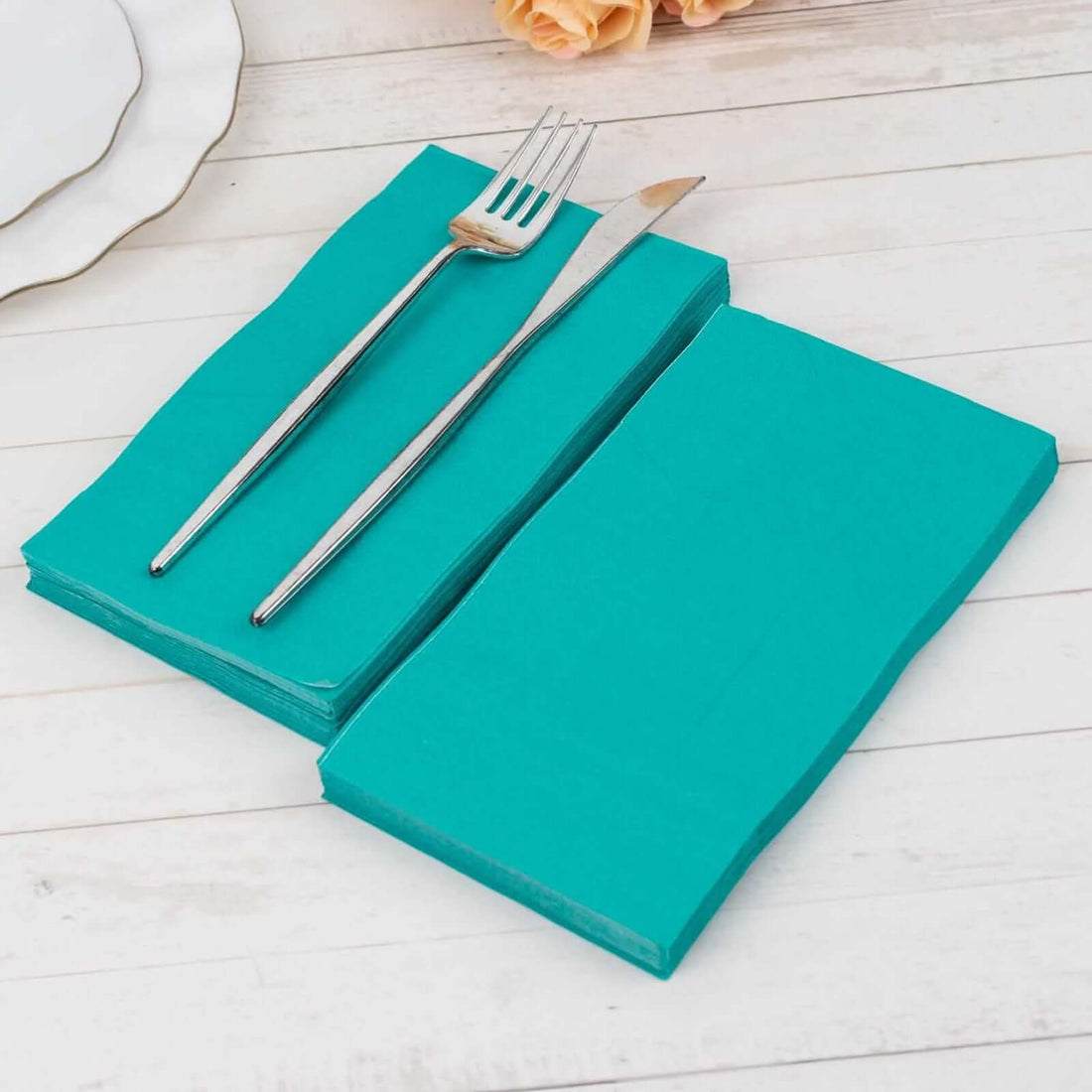 Turquoise napkins with a fork and knife on a wooden table.