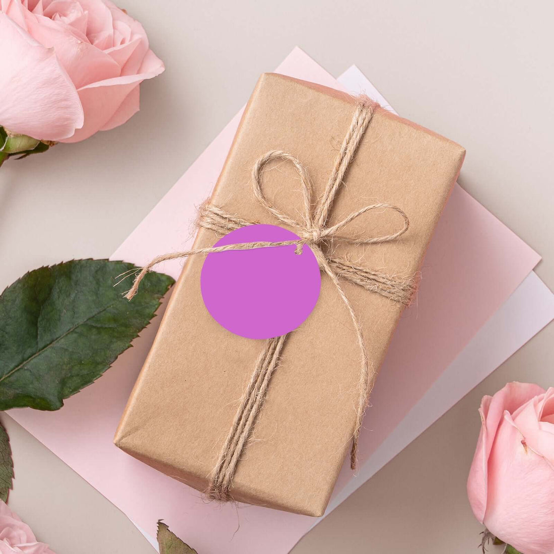 Gift box with twine and pink tag surrounded by roses and decorative paper.