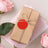 Gift box wrapped in brown paper with a red tag, surrounded by pink roses.