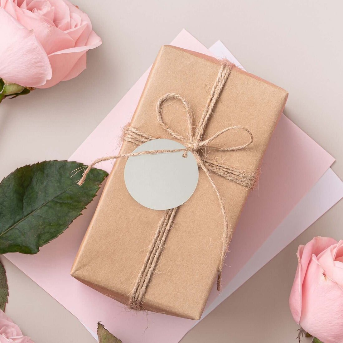 Gift-wrapped package with rustic twine and a blank tag, surrounded by pink roses.