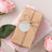 Gift-wrapped package with rustic twine and a blank tag, surrounded by pink roses.