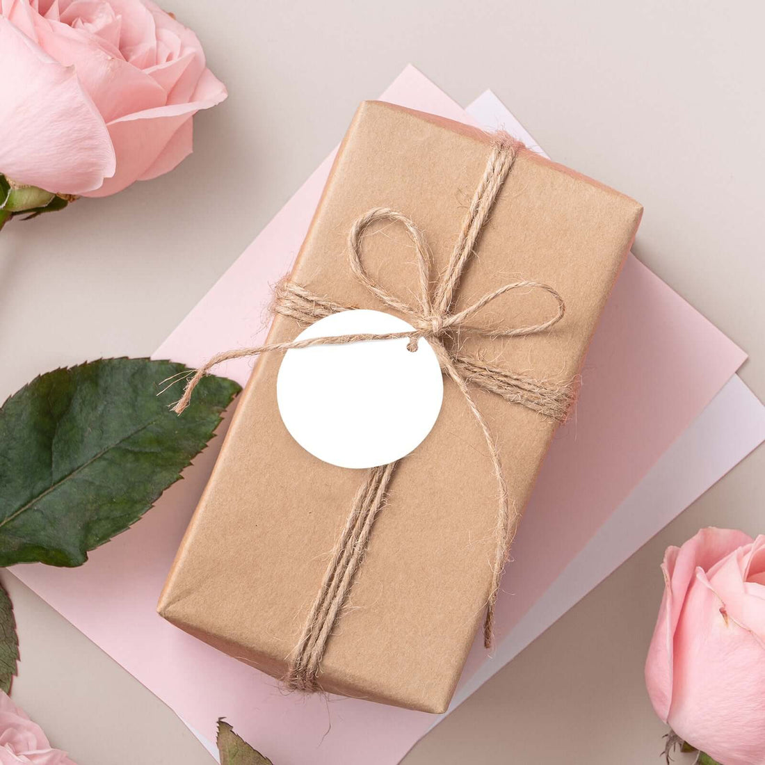 Brown gift box with twine and tag, surrounded by pink roses and paper.