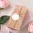 Brown gift box with twine and tag, surrounded by pink roses and paper.