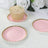 Pink dessert plates with gold trim and a cupcake on a textured surface.