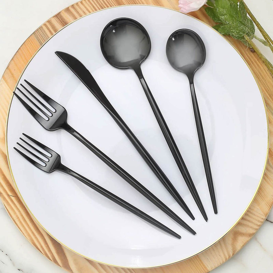 Black plastic cutlery set on a white plate with wooden board background.