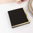 Black notebook with gold corner accents on a white surface.