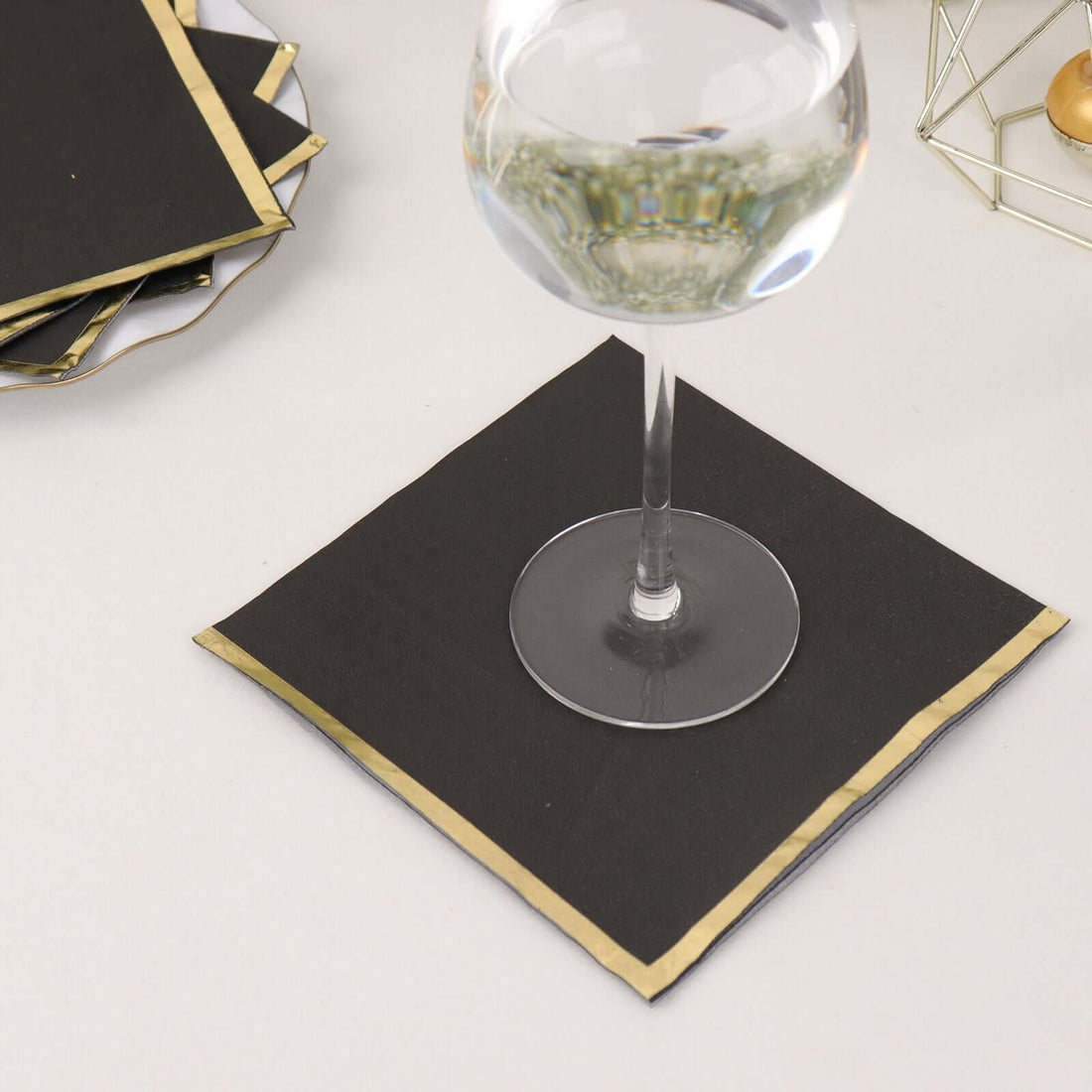 Black napkin with gold trim under a wine glass.