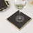 Black napkin with gold trim under a wine glass.
