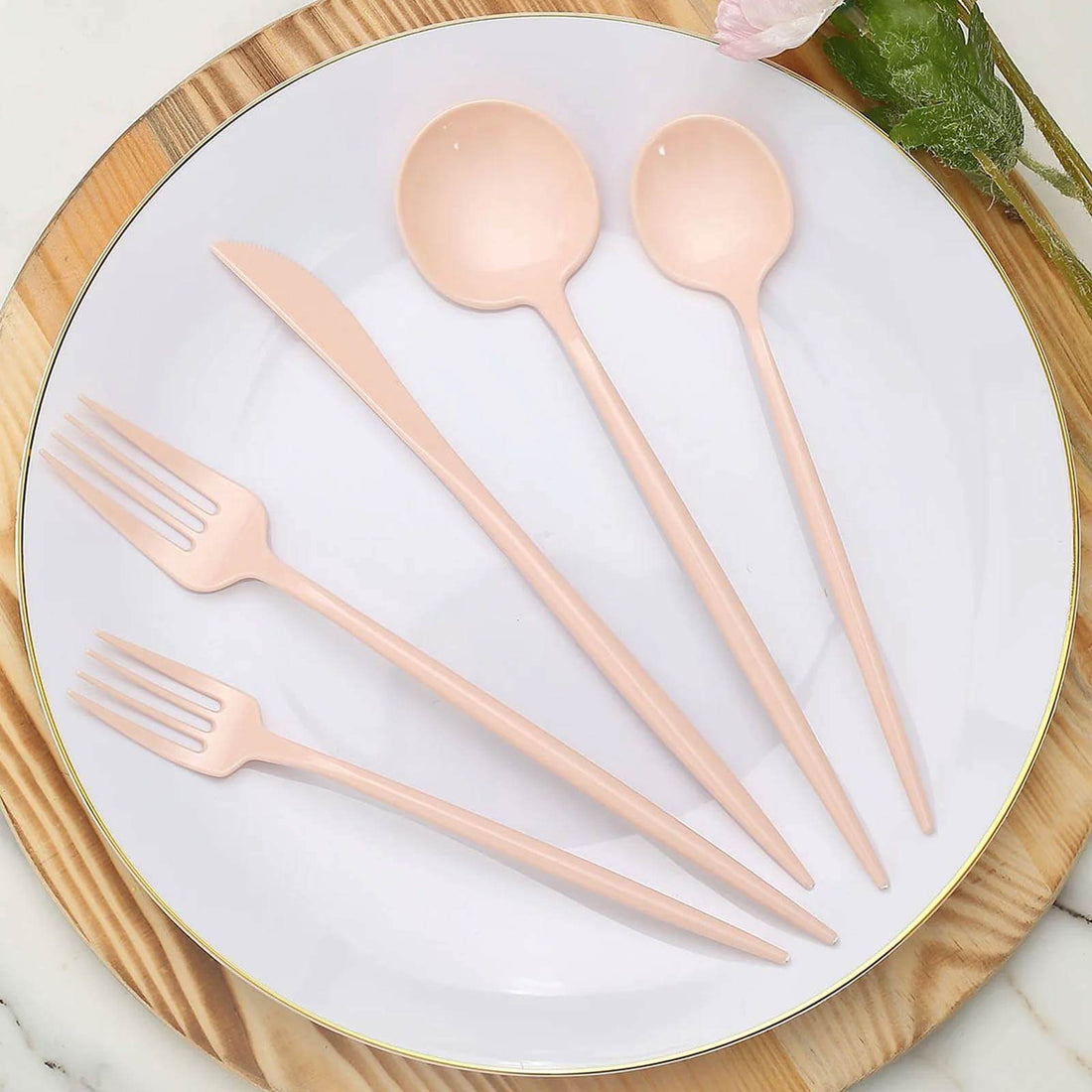 Pink biodegradable cutlery set on a white plate with a wooden background.